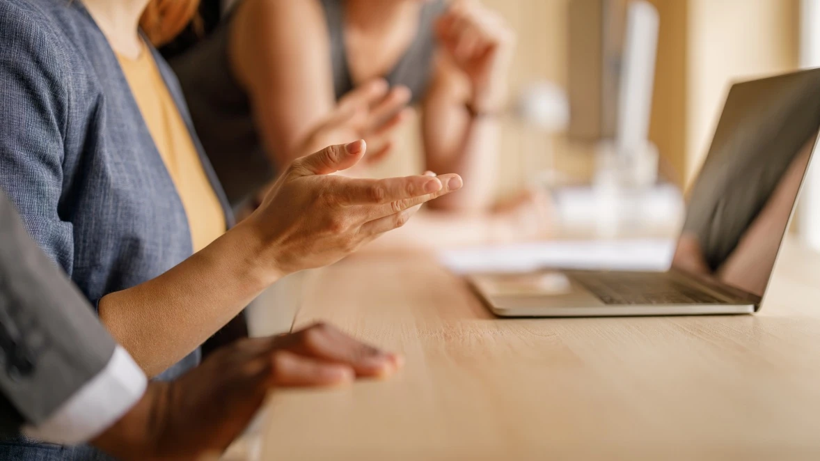 Two colleagues in conversation across a desk with an open laptop