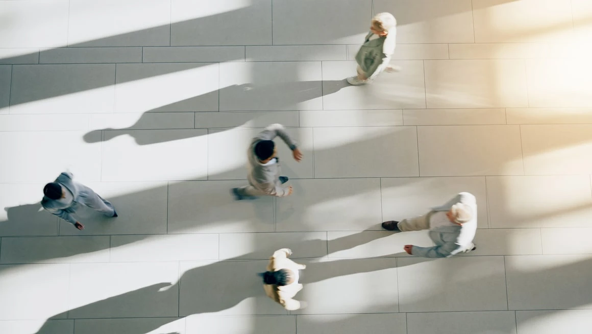 Overhead view of people walking across a sunlit atrium floor, casting long shadows